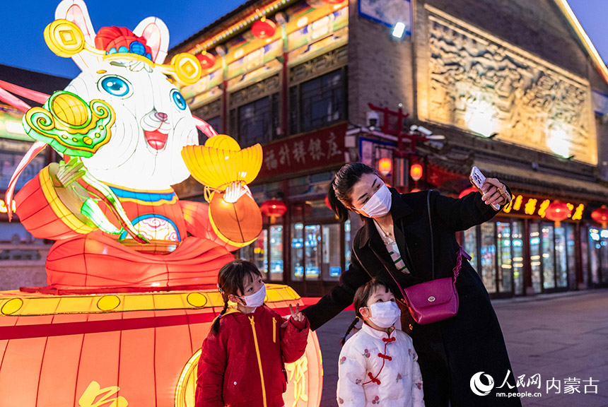 1月18日晚，呼和浩特市玉泉區(qū)塞上老街歷史文化街區(qū)，家長陪伴孩子在“福兔賀春”花燈前拍照打卡。丁根厚攝