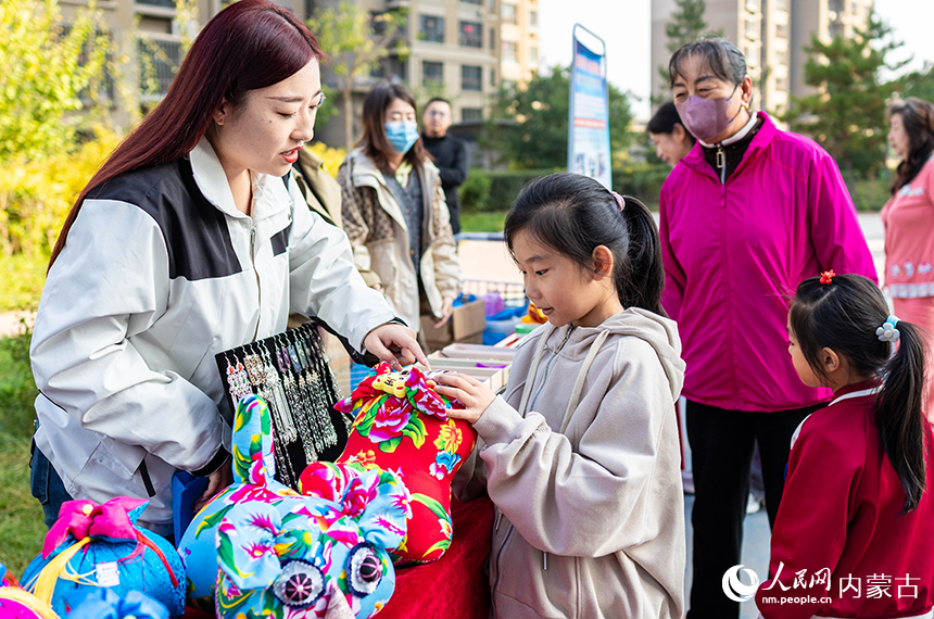 呼和浩特市玉泉區(qū)“文明市集”主題活動(dòng)現(xiàn)場(chǎng)，工作人員為小朋友講解“敕勒川巧娘”布老虎手工藝品的制作技藝。丁根厚攝