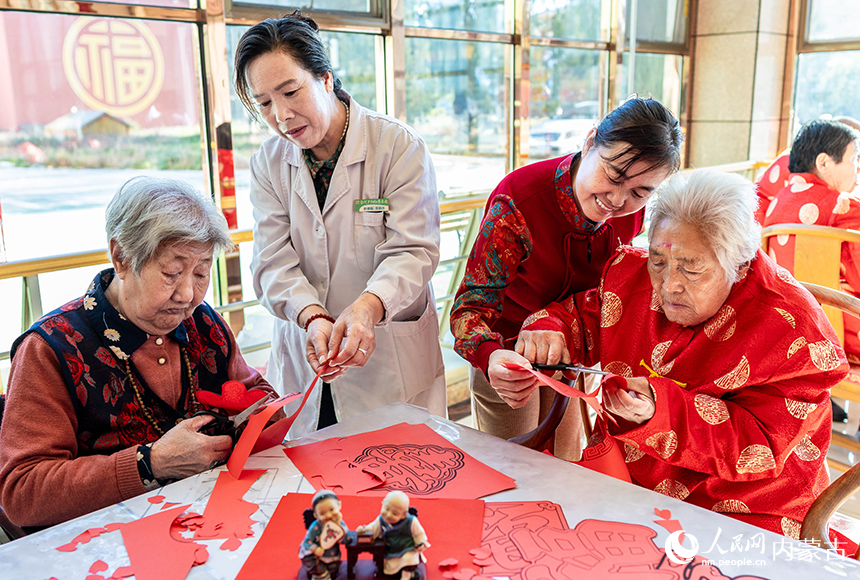 護理員陪伴老人們在呼和浩特市玉泉區(qū)民政局“愛心敬老 情暖重陽”主題活動現(xiàn)場一起剪紙。丁根厚攝