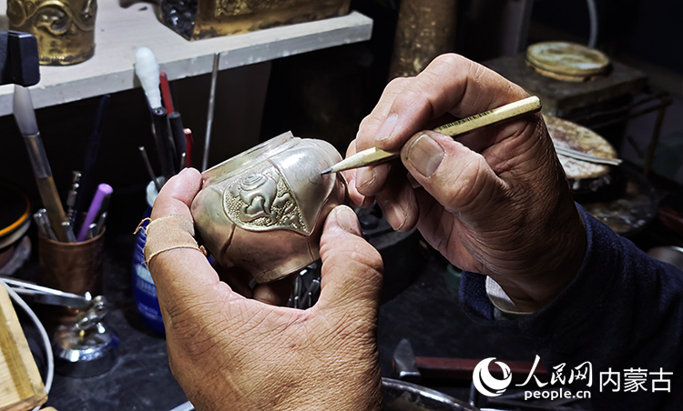 國家級非物質(zhì)文化遺產(chǎn)代表性項(xiàng)目烏拉特銅銀器制作技藝傳承人巴圖陶高對需要鏨刻的銀壺設(shè)計(jì)圖案。人民網(wǎng)記者 張雪冬攝