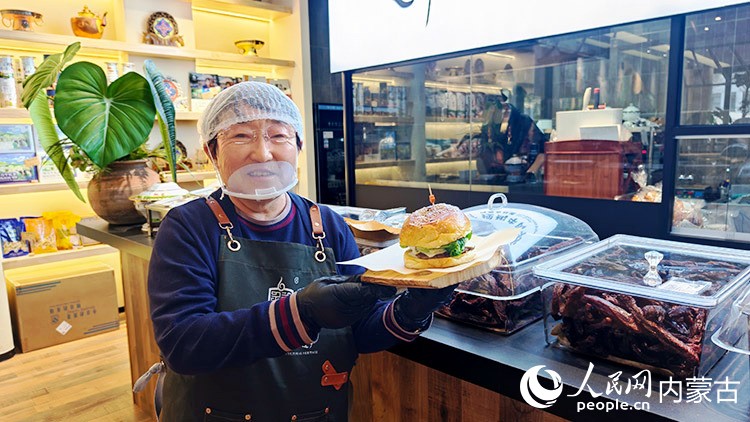非遺代表性技藝“炭烤牛肉干”傳承人白秀枝展示她做好的“蒙古漢堡”，店內(nèi)可制作的還有包括牛肉干、奶皮子等產(chǎn)品。人民網(wǎng)記者 張力洋攝